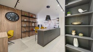 A modern kitchen with a central island, wooden wall paneling, and a black clock.
