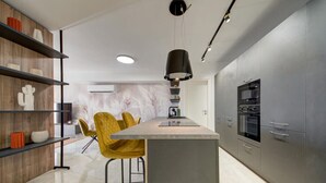 A modern kitchen with a central island, grey cabinetry, and a yellow chair.