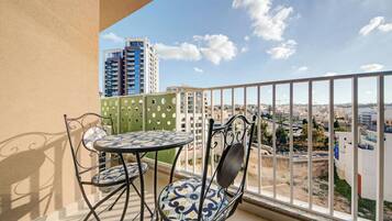 A balcony with a table and chairs, offering a view of a cityscape with buildings and a clear sky.