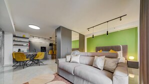 Ein modernes Wohnzimmer mit grauem Sofa, gelben Sesseln, einem Essbereich und einer grünen Akzentwand.