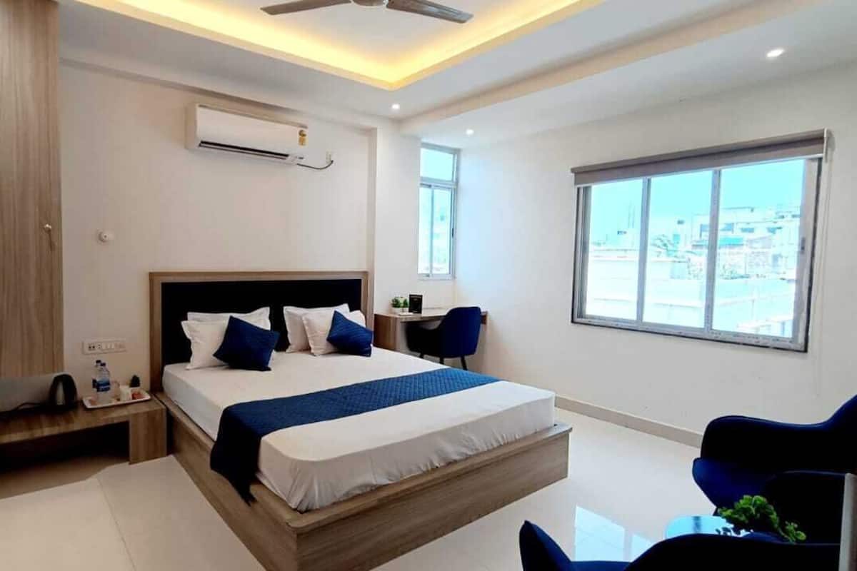 A modern hotel room with a large bed, bedside tables, a desk, and a window with a city view.