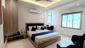 A modern hotel room with a large bed, bedside tables, a desk, and a window with a city view. - Lakhdatar Hotel (Deoghar)