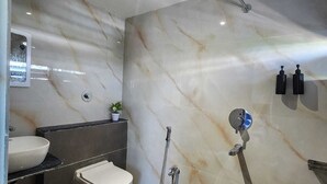 A modern bathroom with a marble wall, a toilet, a sink, and a shower. - Lakhdatar Hotel (Deoghar)