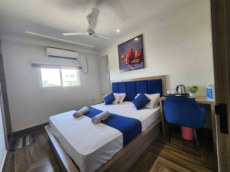 Habitación de hotel con una cama, un escritorio, una silla, un ventilador de techo, un equipo de aire acondicionado, una ventana y un cartel en la pared.