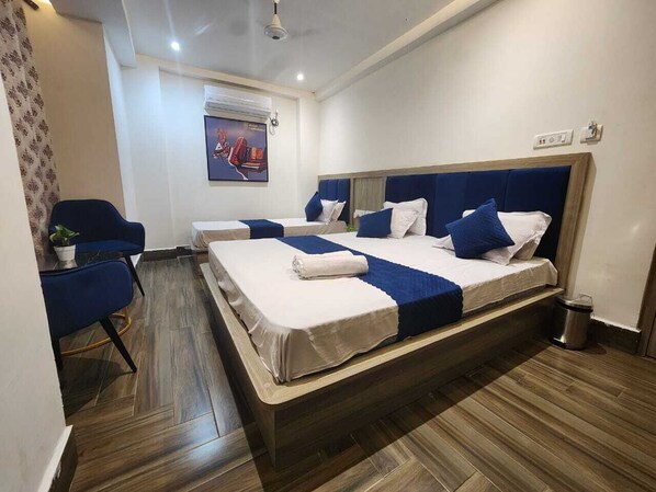A hotel room with two beds, a blue chair, a small table, and a potted plant. - Lakhdatar Hotel (Deoghar)