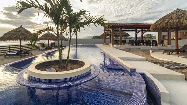 Una piscina con un design circolare, palme e ombrelloni di paglia.