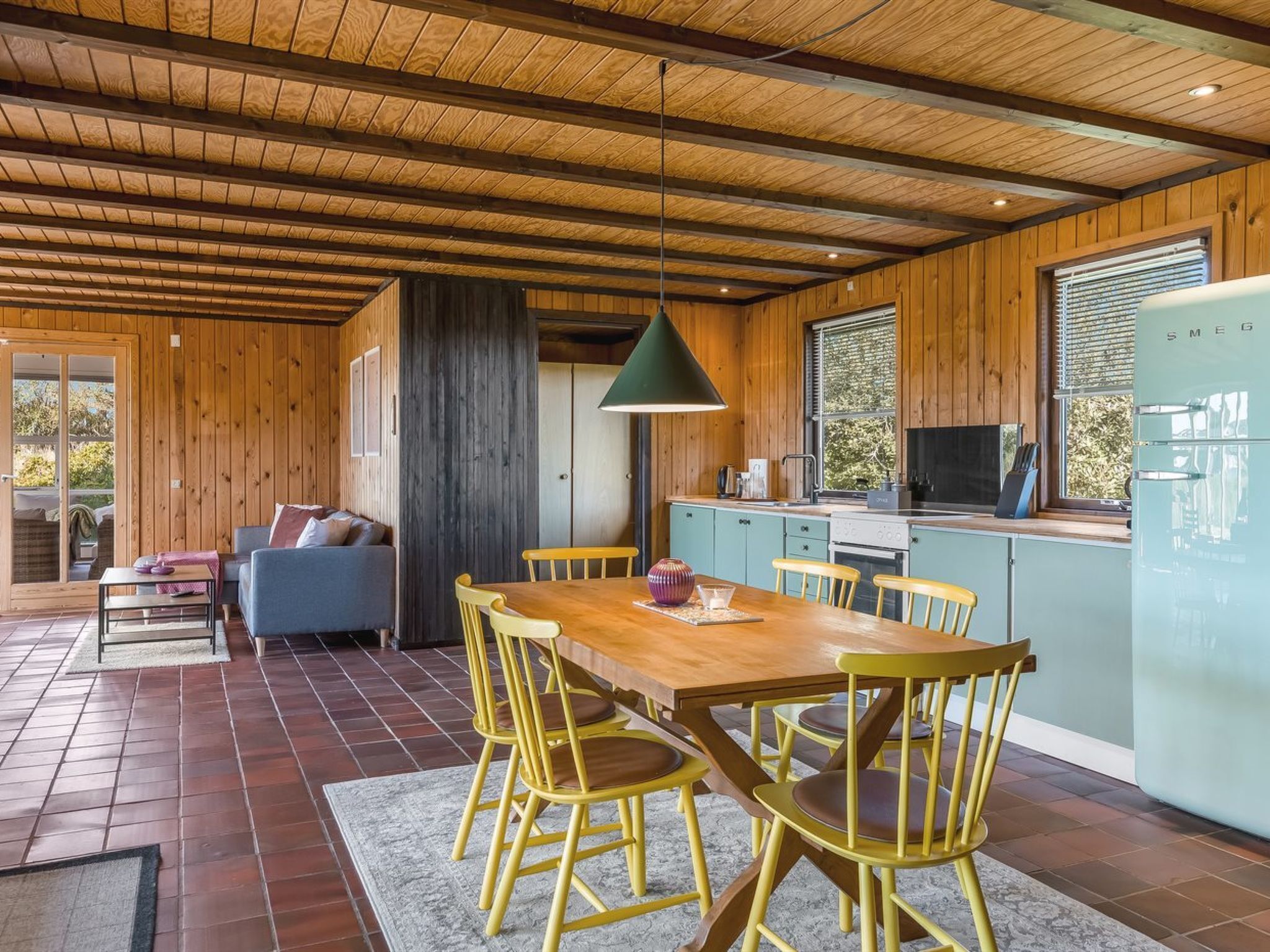 Un intérieur en bois comprenant un coin repas, une cuisine et une grande fenêtre.