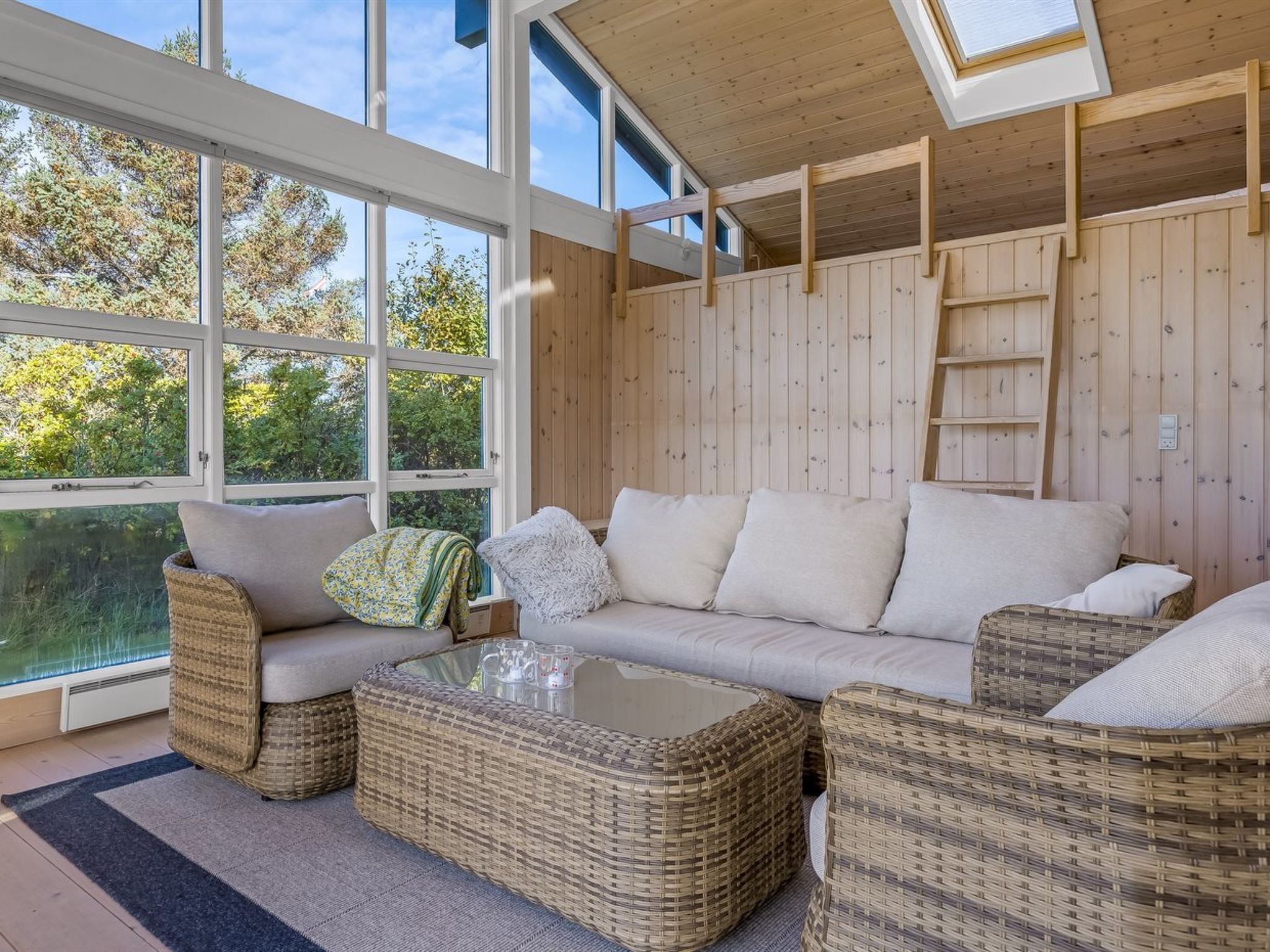 Une pièce chaleureuse avec une grande fenêtre, des meubles en osier et un décor intérieur en bois.