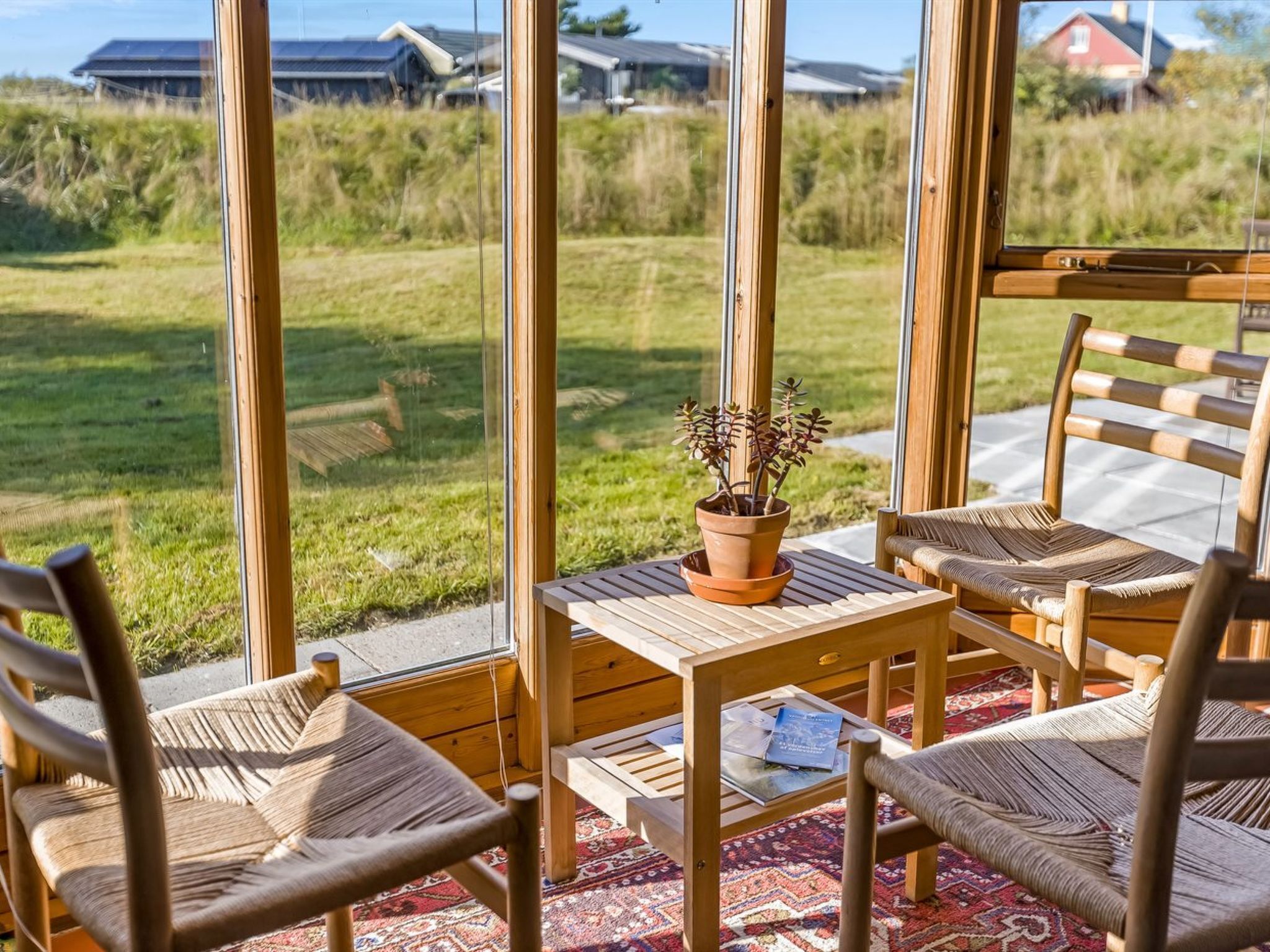 A wooden deck with a table and chairs, a potted plant, and a view of a grassy area with houses in the background.