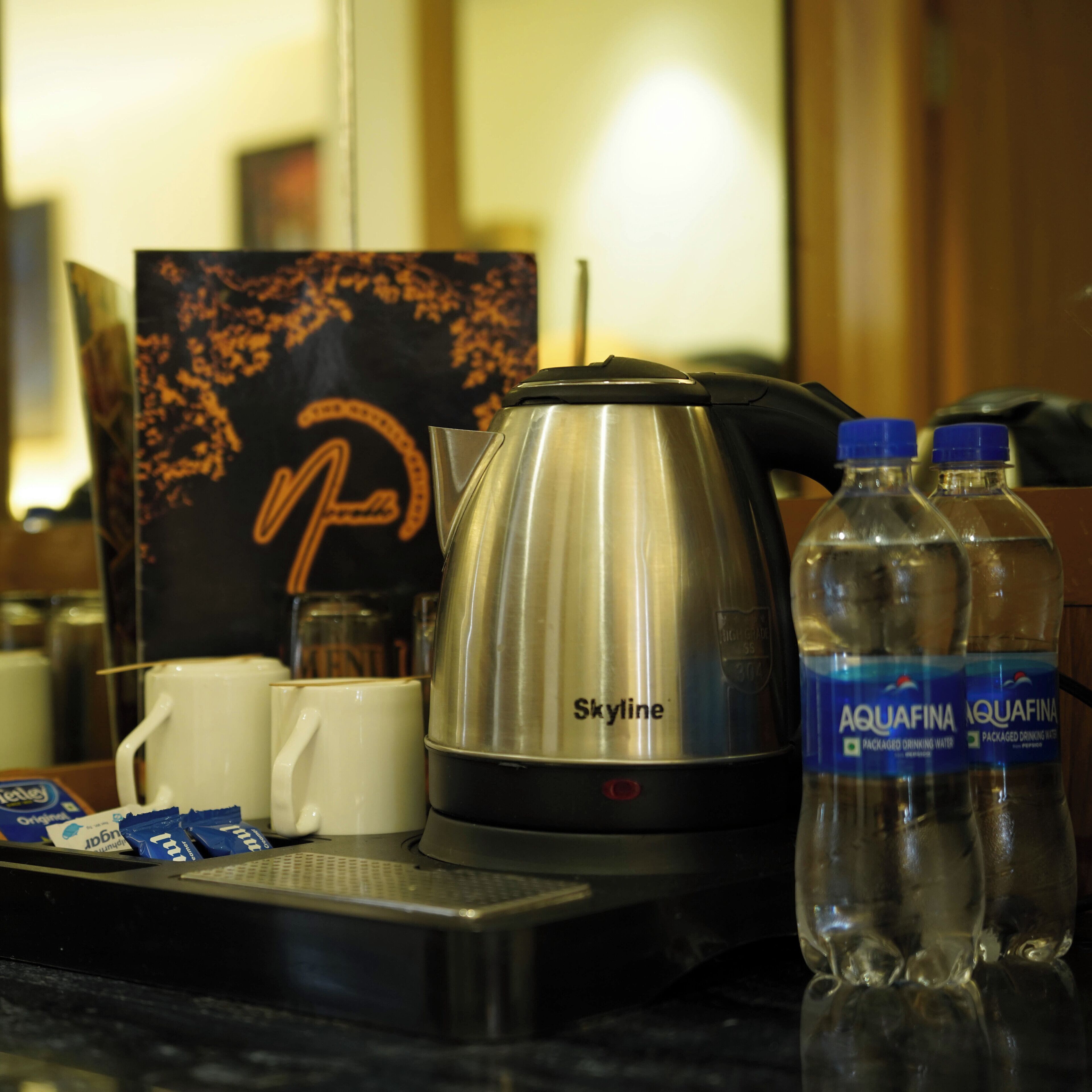 A kitchenette with a stainless steel kettle, two water bottles, a coffee maker, and a coffee pod.