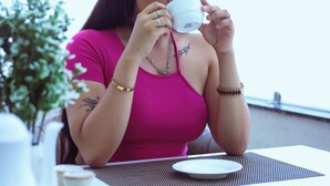 Eine Person sitzt an einem Tisch mit Tasse, Teller und einer kleinen Pflanze.