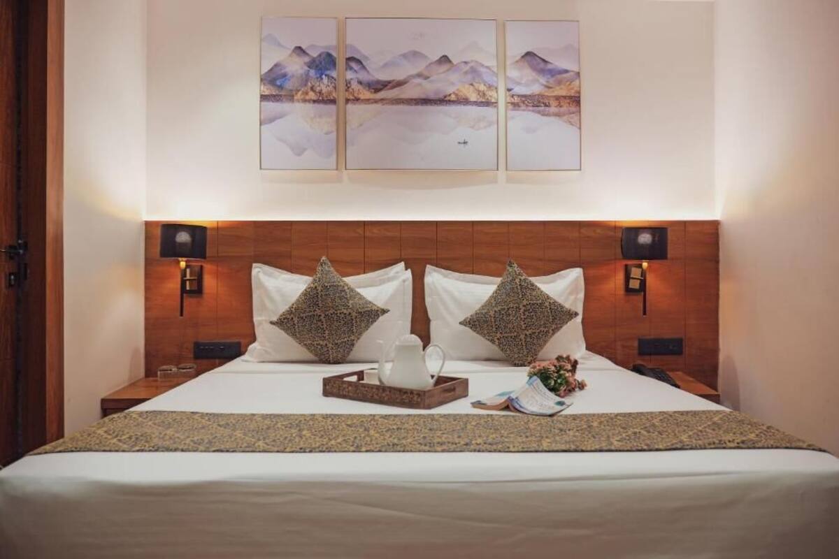 A neatly made bed with a wooden headboard, two decorative pillows, a tray with a white pitcher, and a small table with a book and flowers.