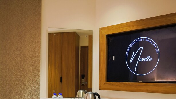 Ein Hotelzimmer mit einem Holztisch, einem Sessel, einem kleinen Tisch mit einer Vase, einem an der Wand befestigten Fernseher und einem Spiegel.