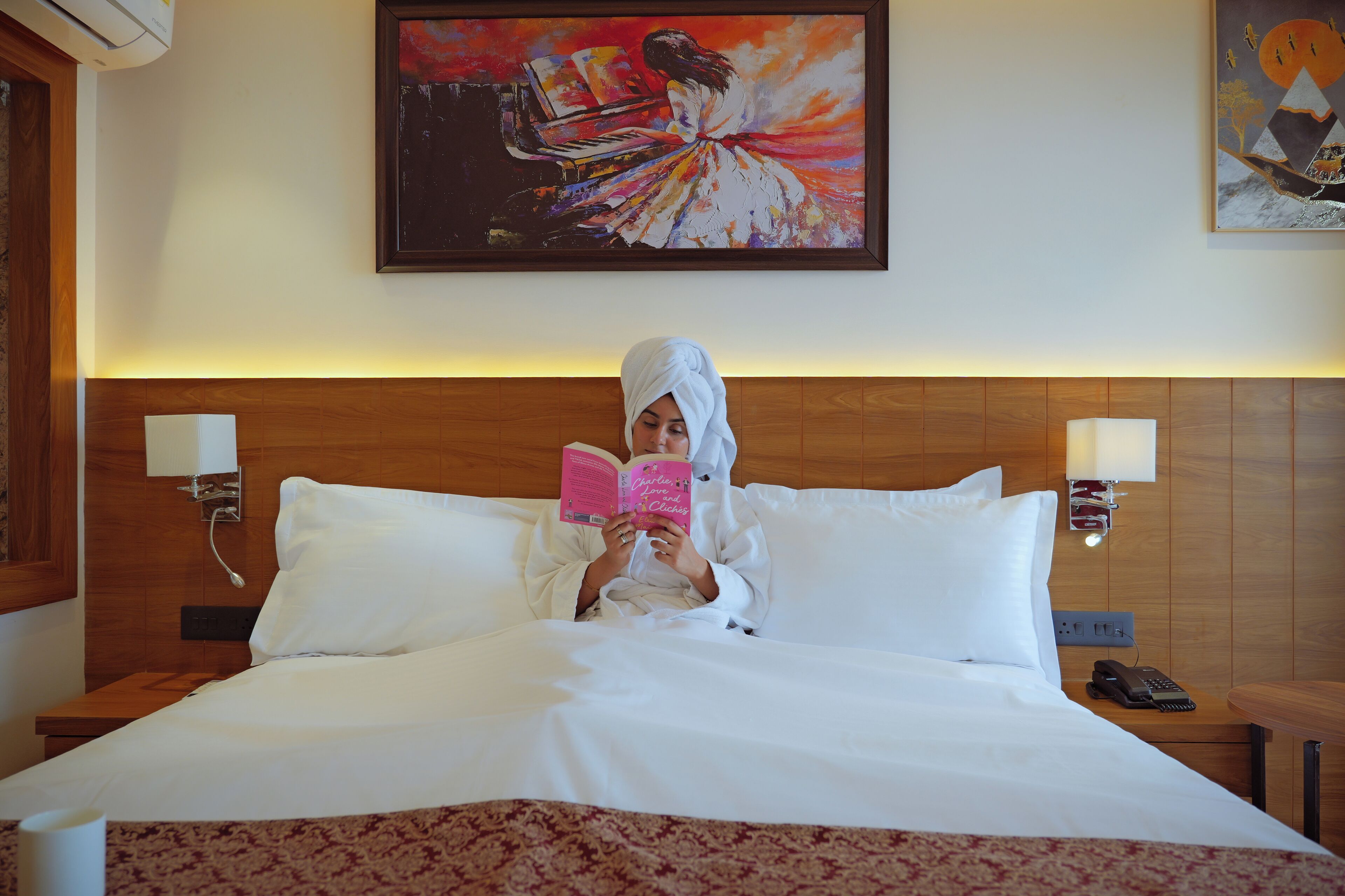 Ein Hotelzimmer mit Bett, Leselampe, Telefon und einem Gemälde an der Wand.
