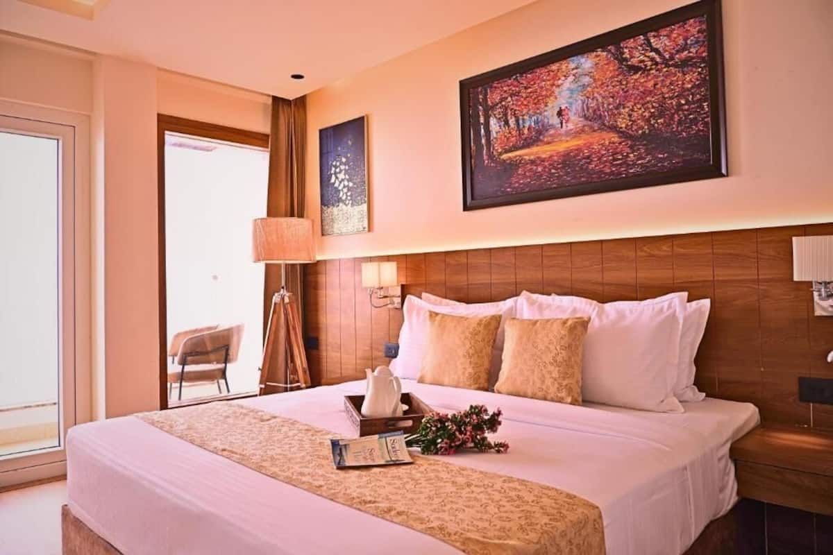 A hotel room with a large bed, a wooden headboard, a painting on the wall, and a window with a view.