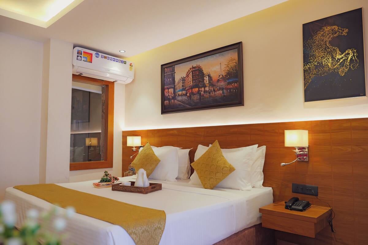 A hotel room with a large bed, two bedside lamps, a nightstand with a phone, and a wall-mounted air conditioner.