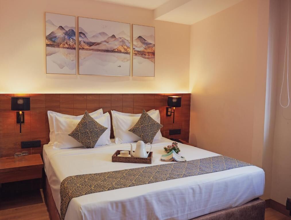 A hotel room with a large bed, wooden headboard, and three wall-mounted paintings.
