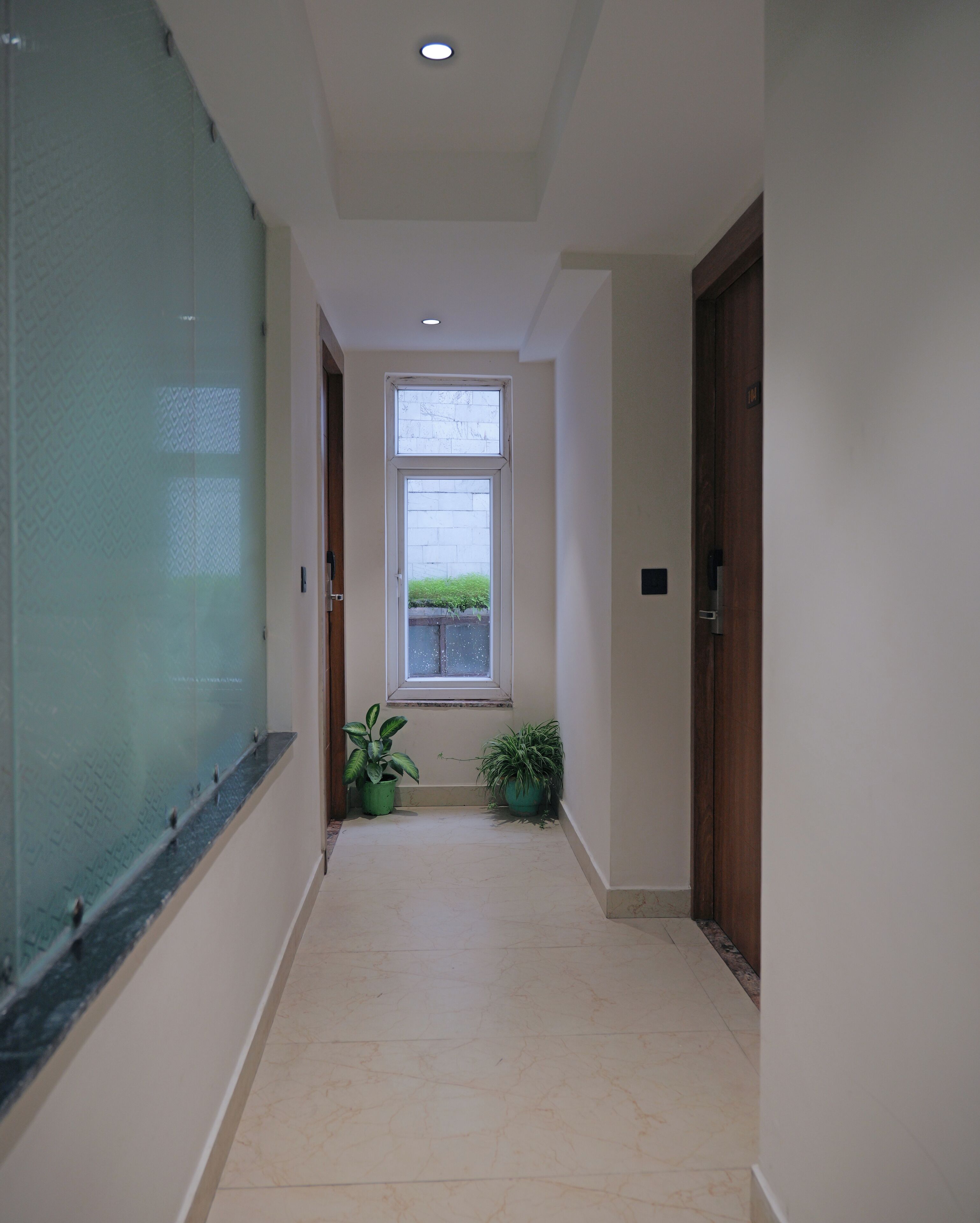 A hallway with a tiled floor, a glass wall on the left, and a door on the right.