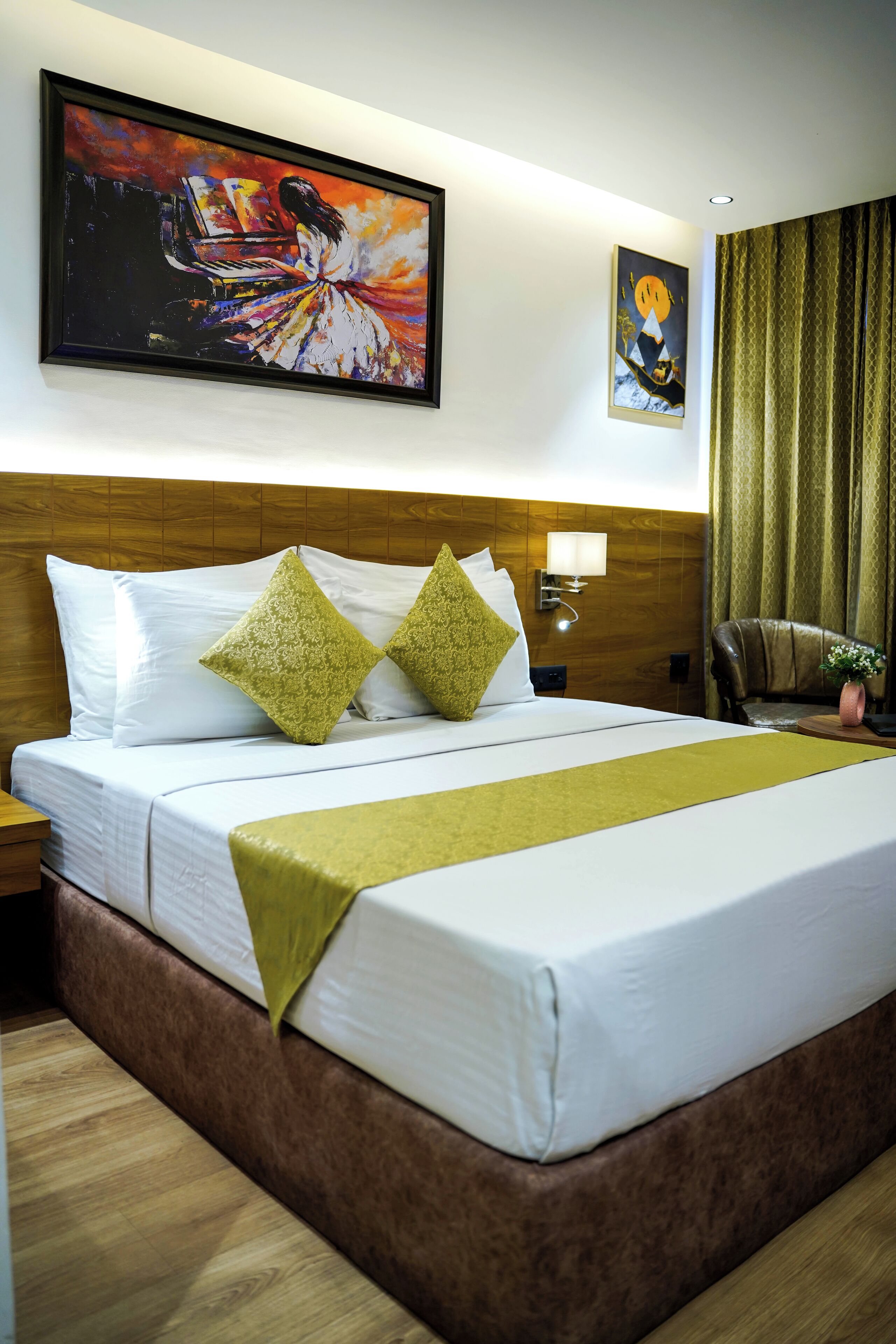 Une chambre d’hôtel avec un grand lit, deux oreillers, une table de chevet, une lampe, une chaise et deux tableaux au mur.