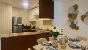 Eine moderne Küche mit integriertem Kühlschrank, Mikrowelle und Kaffeemaschine. Ein Essbereich mit einem Marmortisch, gedeckt für vier Personen, blaues Servietten und eine Vase mit weißen Blumen.