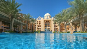 Ein Hotel mit großem Pool, Palmen und einem zentralen Gebäude mit Kuppel und Bögen.