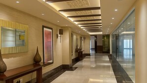 Ein Hotelgang mit poliertem Marmorboden, eingelassener Beleuchtung, einer Rezeption und einem Glaselevator.