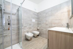 Ein modernes Badezimmer mit einer Duschkabine aus Glas, einem Bidet, einer Toilette und einem hölzernen Waschtisch.