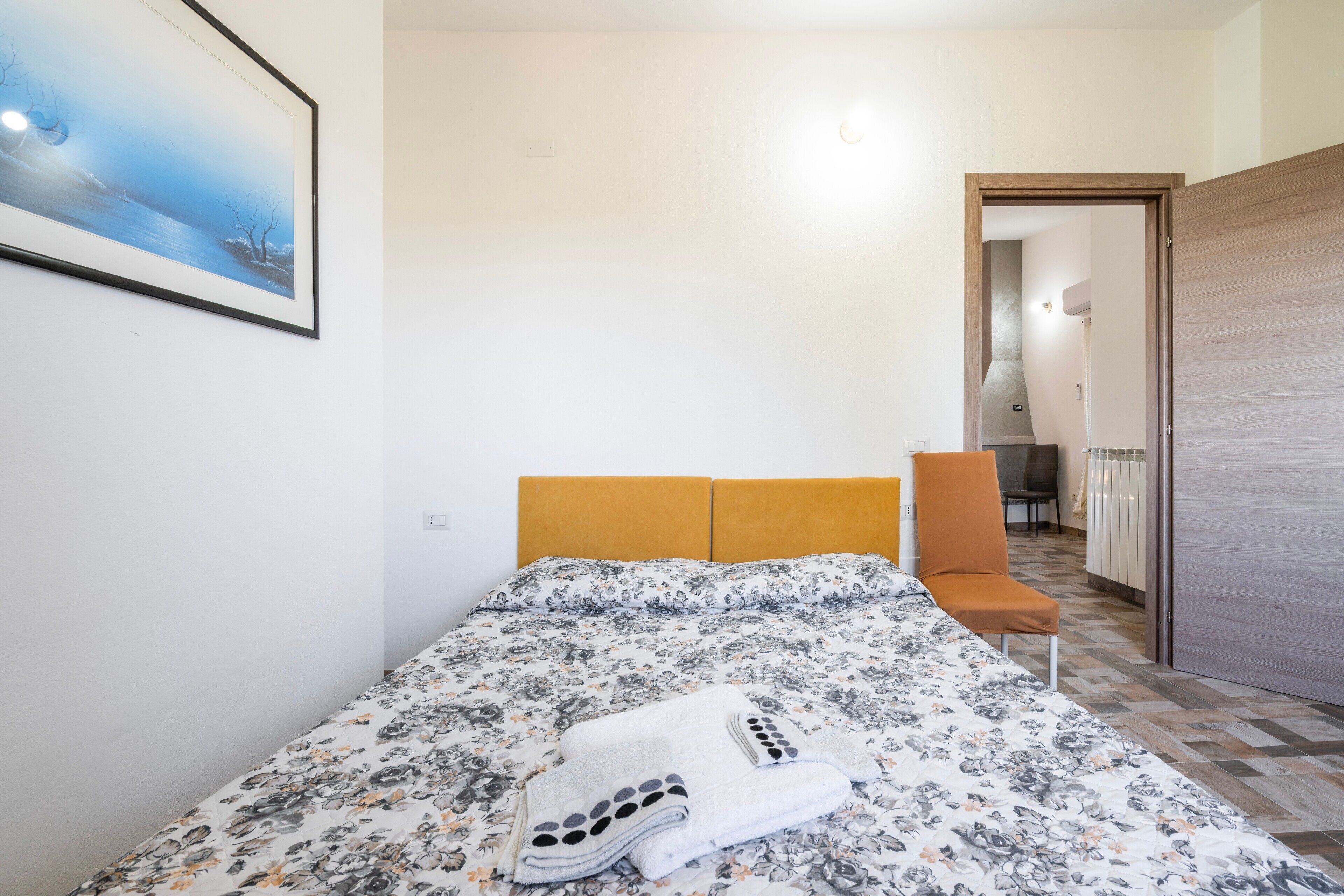 Un dormitorio con una cama, una silla, un cuadro y una puerta que da a otra habitación.