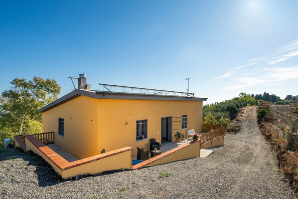 A single-story yellow building with a covered patio, a small outdoor seating area, and a gravel driveway.