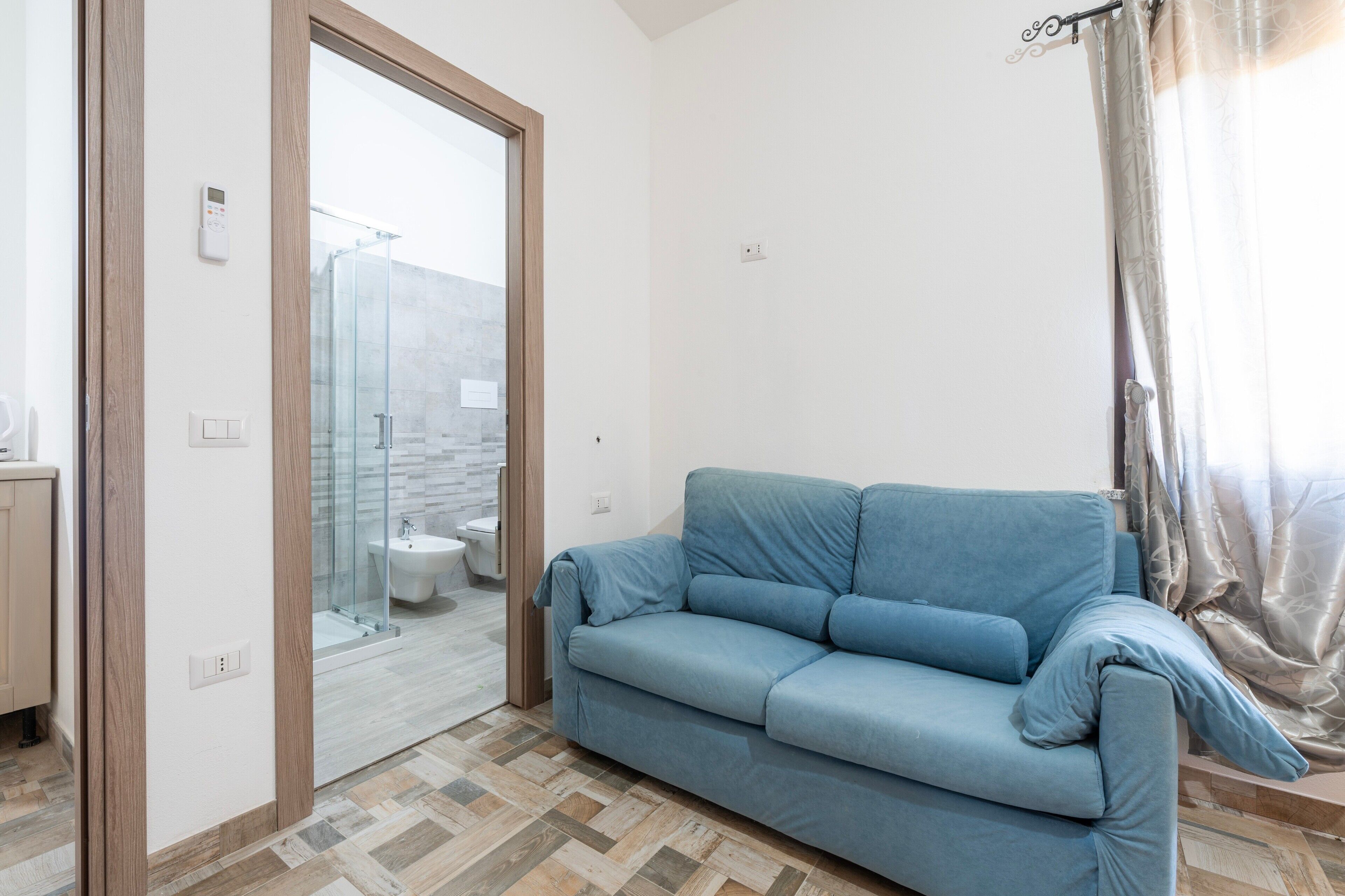 A modern bathroom with a glass shower enclosure, a toilet, and a blue sofa in a living area.
