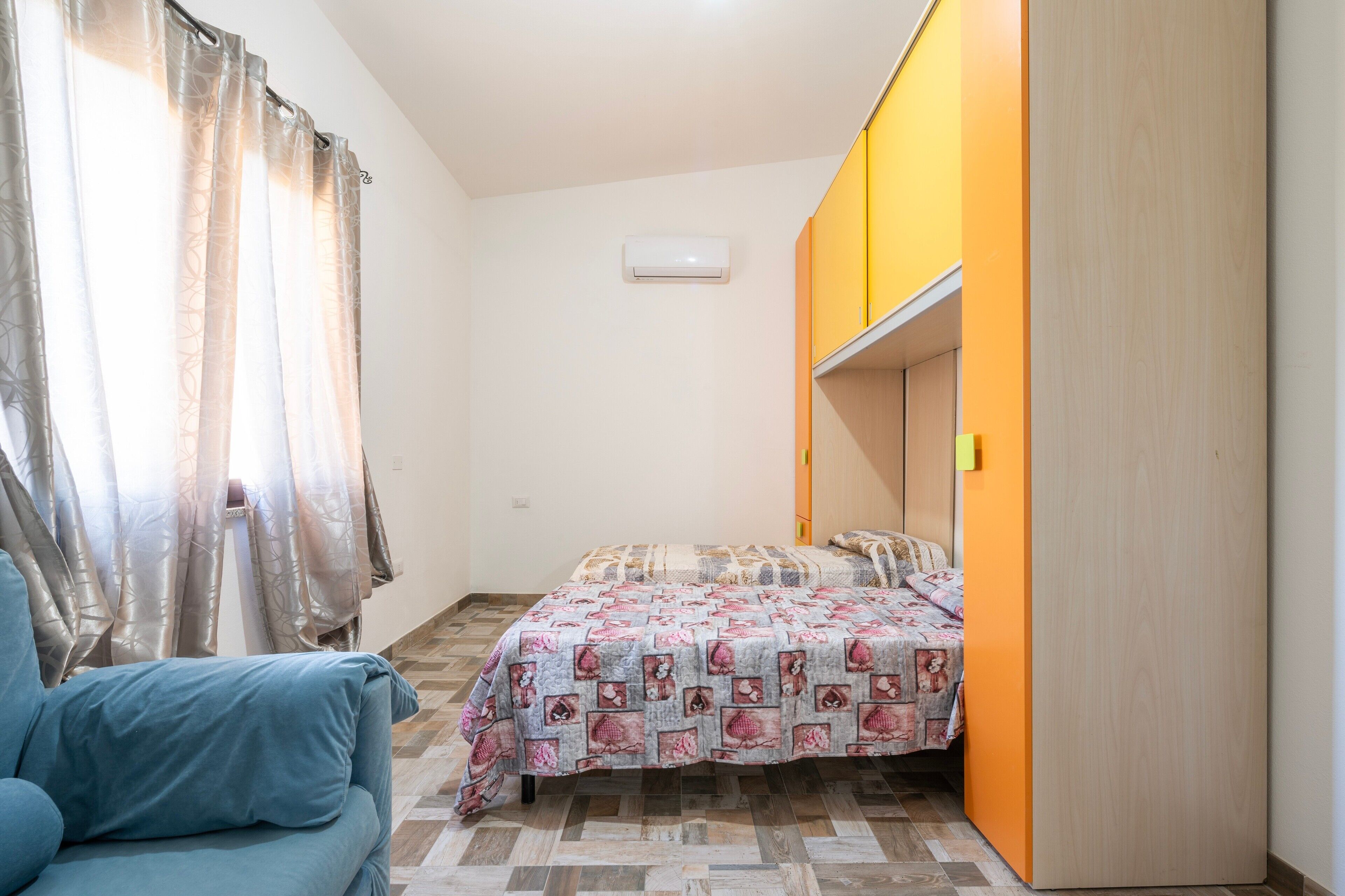 Un dormitorio con cama, armario, ventana con cortinas y aire acondicionado instalado en la pared.