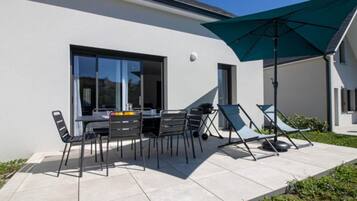 An outdoor patio with a table and chairs, a green umbrella, and a sun lounger.