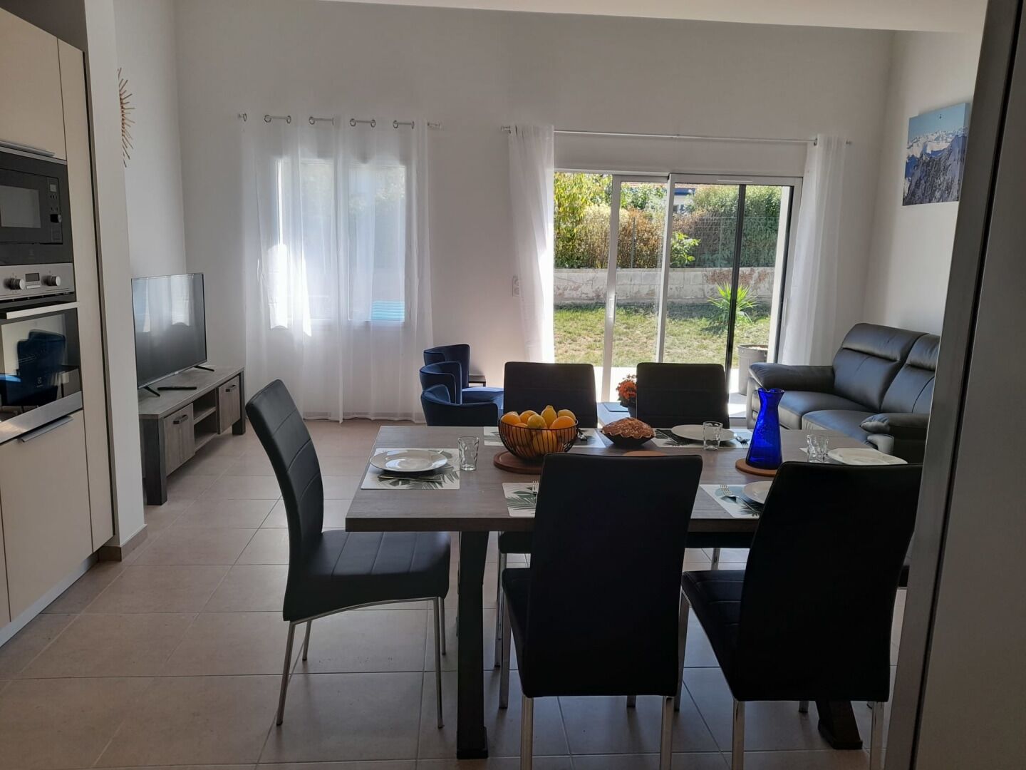 A modern kitchen with a dining area, a TV, and a view of the outdoors.