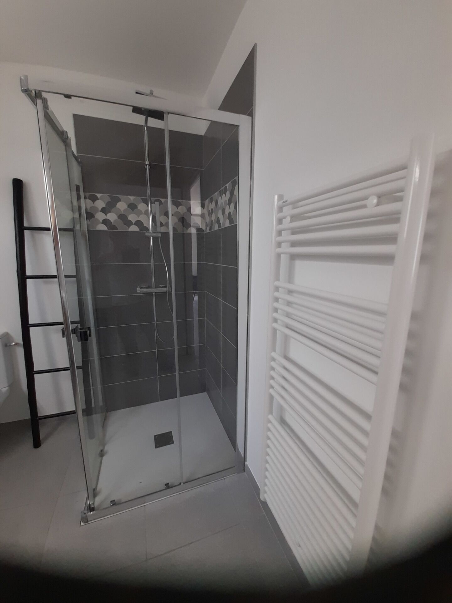 Une douche fermée par des parois de verre, avec un sol carrelé et un porte-serviettes blanc.