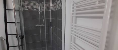 Une douche fermée par des parois de verre, avec un sol carrelé et un porte-serviettes blanc.