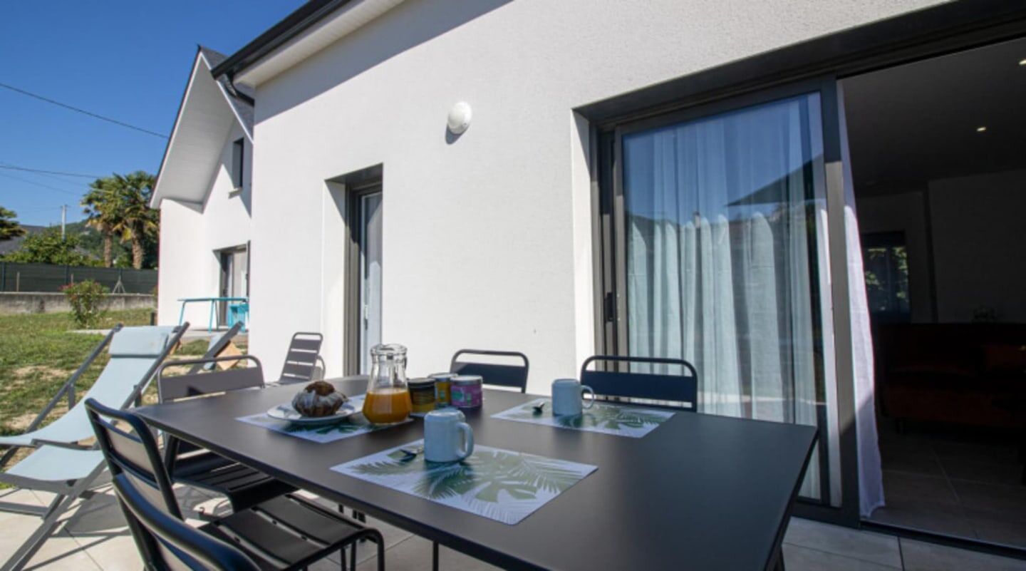 An outdoor dining area with a table set for breakfast, a patio chair, and a sliding glass door leading to a pool.