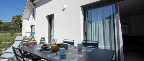An outdoor dining area with a table set for breakfast, a patio chair, and a sliding glass door leading to a pool.