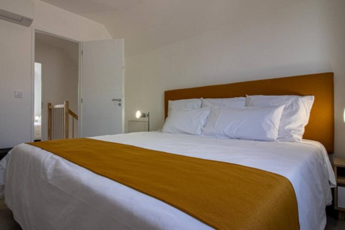Une chambre d’hôtel avec un grand lit, une tête de lit en bois, une table de chevet et une porte donnant sur une autre pièce.