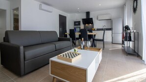 Een moderne woonkamer met een grijze bank, een witte salontafel met een schaakbord, en een keuken op de achtergrond.