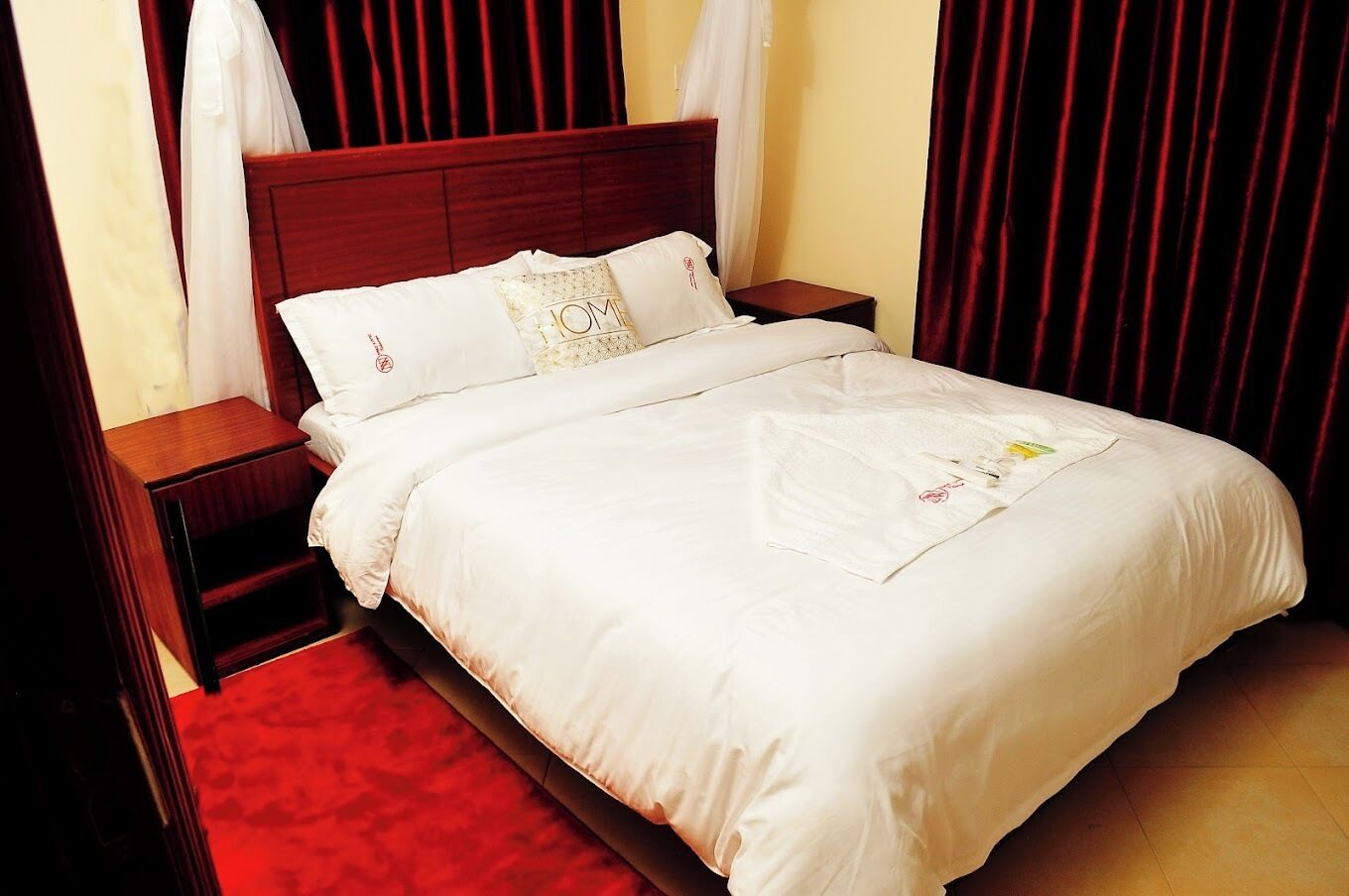 Una cama bien hecha con sábanas blancas, un cabecero de madera y una mesita de noche con una lámpara.