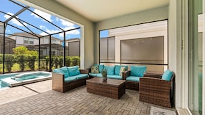 Un patio techado con mobiliario de mimbre, una piscina y vistas a casas vecinas.