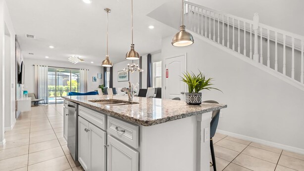 A modern kitchen with a large island, pendant lights, and a staircase leading to a balcony.