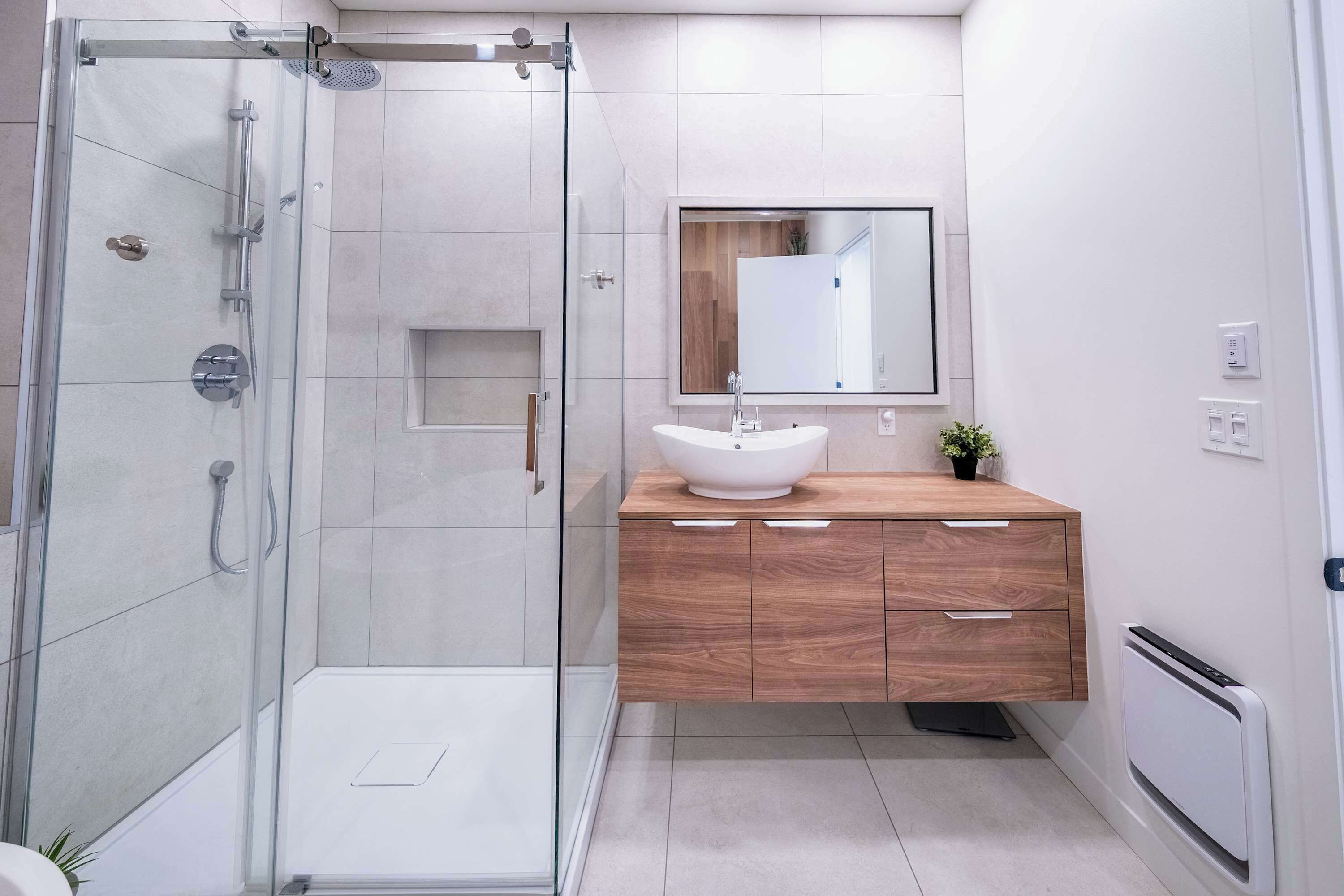 Un bagno moderno con doccia vetrata, mobile bagno in legno con lavabo bianco e uno specchio grande.