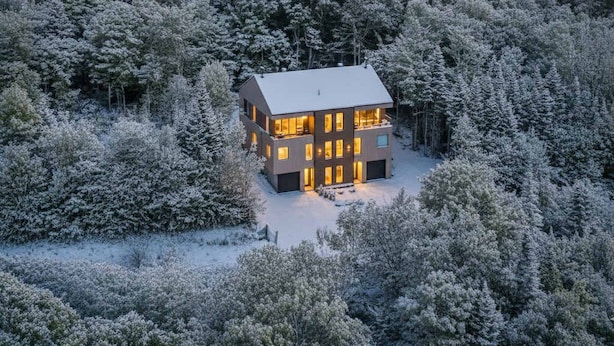 Een modern herenhuis omgeven door een dicht bos met sneeuwbedekte bomen.