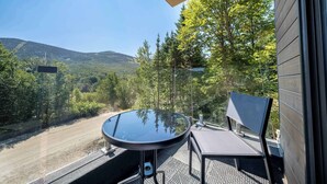 Een balkon met een ronde tafel en een stoel, met uitzicht op een bebost gebied met een weg en heuvels in de verte.