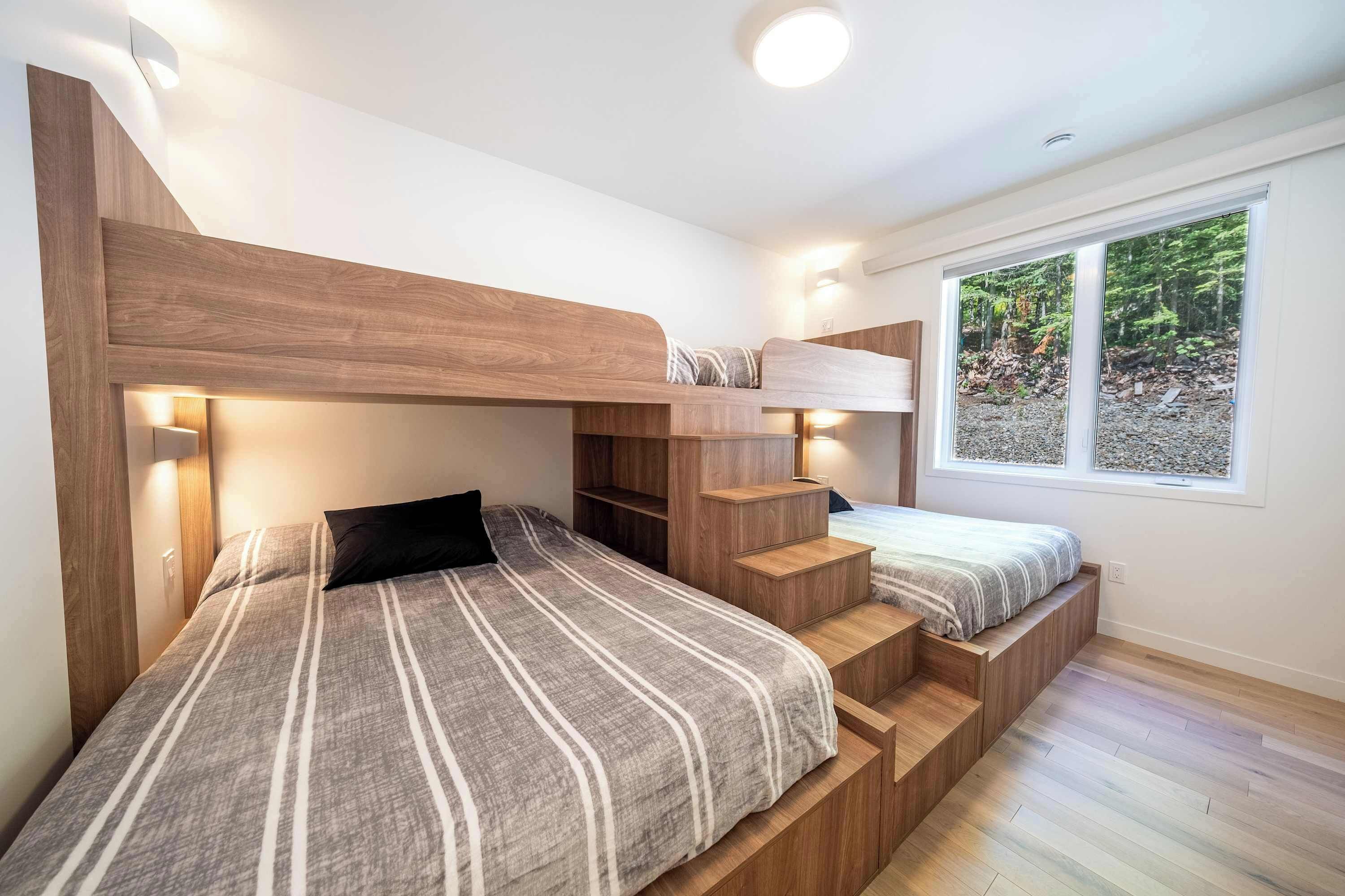 Une chambre moderne avec un lit superposé, des étagères intégrées et une fenêtre donnant sur la forêt.