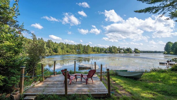 Een houten steiger met stoelen met uitzicht op een meer, omringd door bomen en een heldere lucht.