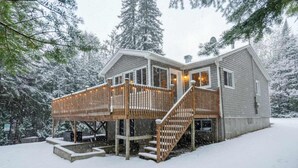 Een houten chalet met een terras en wenteltrap, omringd door met sneeuw bedekte bomen.