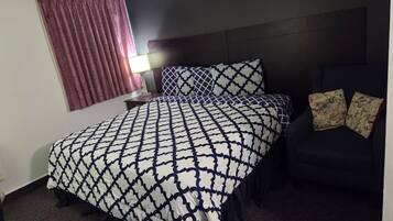 Una camera d'albergo con un letto, un comodino, una lampada e una poltrona scura.