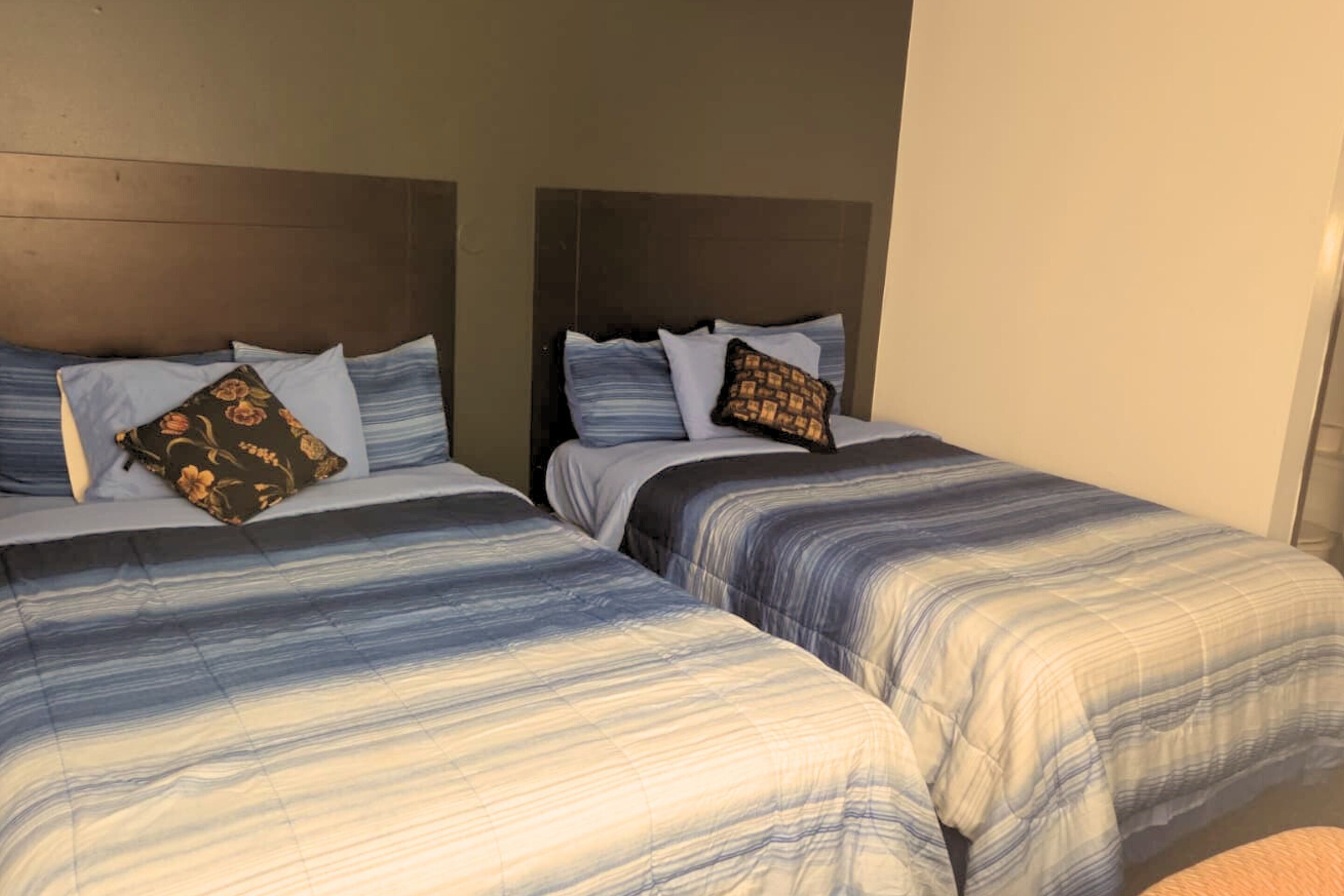 Two beds with striped bedding and matching pillows, a wooden headboard, and a plain wall.